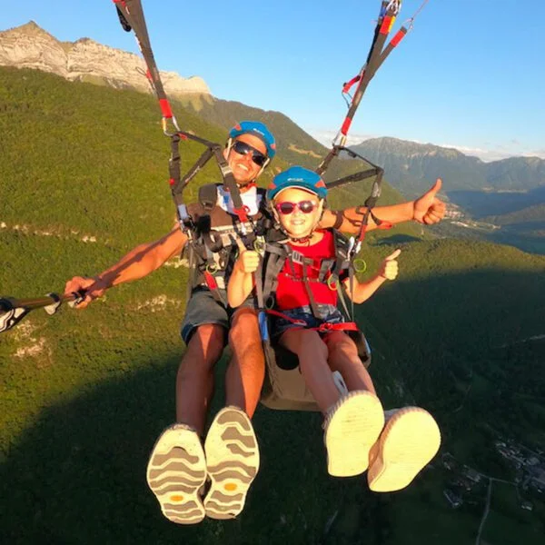 Enfant et son moniteur en plein ciel pour un baptême de parapente à Annecy