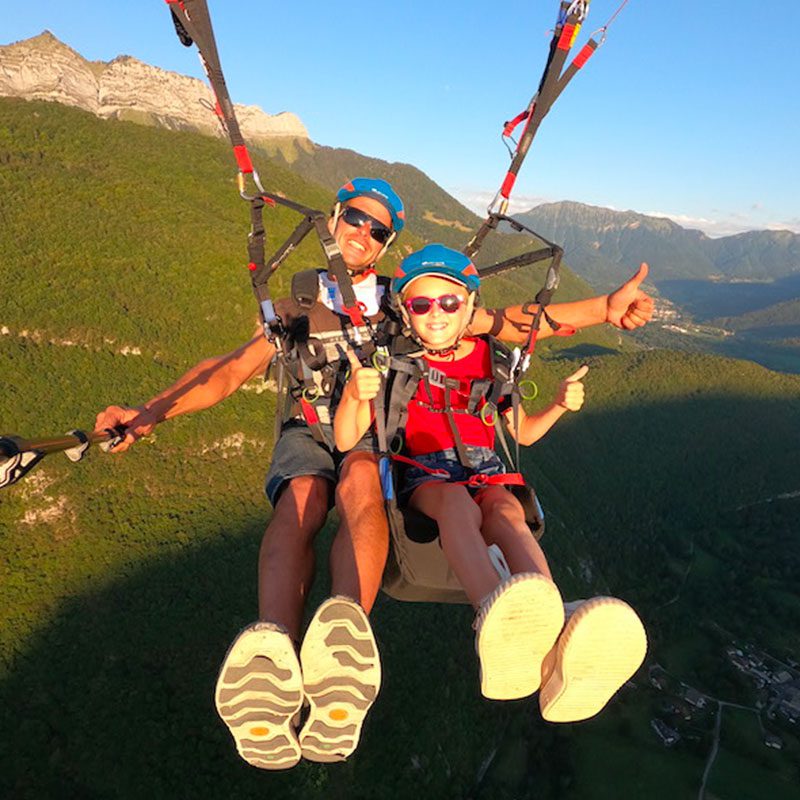 Enfant et son moniteur en plein ciel pour un baptême de parapente à Annecy